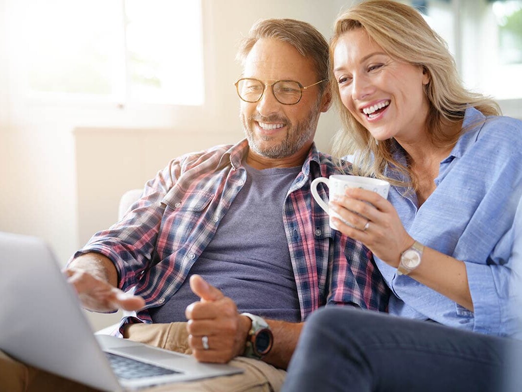 Middle aged couple on laptop smiling with coffee cup